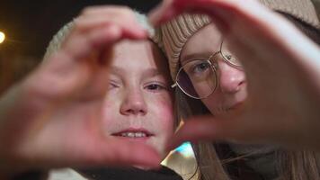 Young mother and her son, both rosy from cold, held their arms in heart shape and looked through them at camera. They were wearing warm winter clothing in midst of winter. Portrait. Close up. video