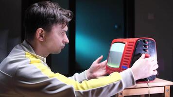 Man frustrated with old portable television set showing static screen. try to adjust tv video