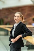 Smiling businesswoman leaning on railing in modern office building photo