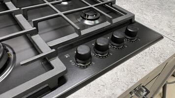 Close-up of a modern gas stovetop with multiple burners and control knobs, set against a textured countertop photo