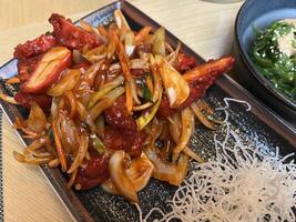 Close up of Sliced chicken fillet with hot garlic sauce with vegetables and fried glass noodle and a bowl of seaweed salad photo