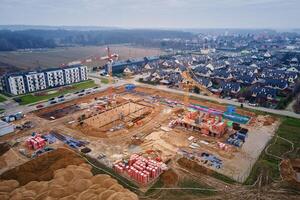 Aerial view of residential buildings under construction surrounded by completed homes and apartments. Cranes, foundations and building materials at construction site. New neighborhood in small town photo
