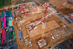 Aerial view of construction site with cranes, foundations and building materials. Residential building under construction. Progress of new development in small town photo