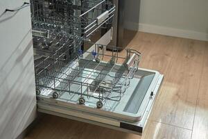 Open empty dishwasher with empty racks and extended basket in modern kitchen ready for loading. Home appliance photo