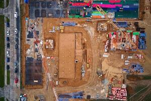 Aerial view of construction site with cranes, foundations and building materials. Residential building under construction. Progress of new development in small town photo