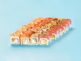 Philadelphia Roll Set with mango, cucumber and avocado, wrapped in perfect seasoned sushi rice and fresh salmon, tuna, shrimp and smoked eel, decorated chili threads. Isolated on light blue background photo