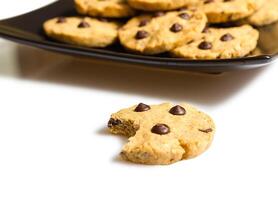 Chocolate cookie with a bite and pile of cookies in a plate on the background photo