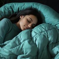 woman sleeping peacefully under cozy aqua blue comforter, exuding tranquility and comfort. soft fabric envelops her, creating serene atmosphere photo
