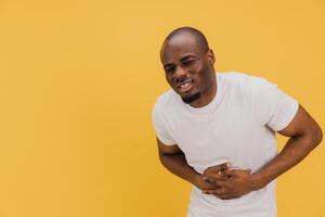 Young African American Man Suffering From Abdominal Pain on Yellow Background photo