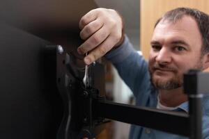 Mounting a TV bracket. A man hangs a TV on a TV bracket on the wall. The mount allows the TV to be turned in any direction for easy viewing from anywhere in the kitchen. photo