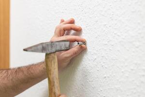 A man uses a hammer to hammer nails. A hammer is the main tool of a builder. High skills in working with a tool do not lead to injuries. Safety concept when working with a hammer photo