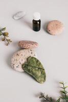 Jade gua sha massager on pebbles, essential oil on table vertical view photo