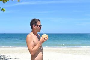 Young man drinking coconut on sandy beach photo