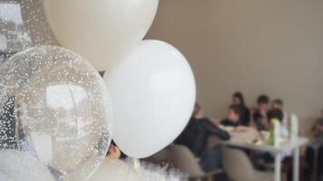 White and beige balloons filled with helium float in air, against the backdrop of festive celebration in honor of child's birthday. Blur, background video