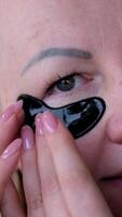 A beautiful woman against black patches under eyes enjoys her self-care routine while wearing under-eye patches. This image embodies the essence of youth and the importance of facial skincare. video