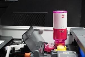 Ink bottles with ink tank printer. Closeup Refilling ink into a red ink tank printer at office. photo
