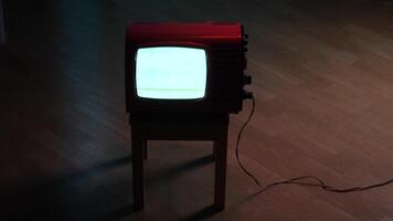 Old red television displaying static noise on wooden stool in dark room video