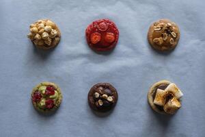 Collection of homemade cookies with different toppings - raspberry, strawberry, pistachio, caramel, chocolate, peanuts, marshmallow, popcorn flavor. photo