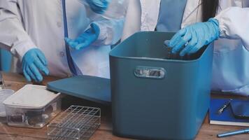 Two people in lab coats and gloves are working on a table video
