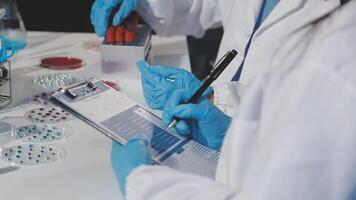 Two people in lab coats and gloves are working on a clipboard video