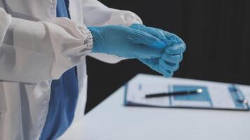 A person in a white coat and blue gloves is holding a clipboard video