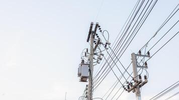 Electrical energy transfer distribution on concrete pole against white sky background, AC high-voltage power transformer, A low angle shot of a power transformer and electrical wires on a metal pole photo
