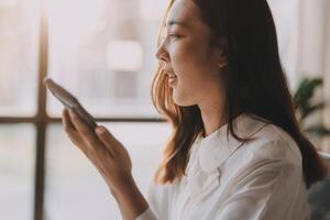 A woman is using her cell phone while sitting in front of a window photo
