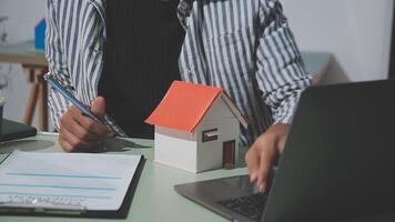A man is working on his laptop and a house model is sitting on the table video