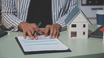 A woman writing on a notepad with a house model in the background video