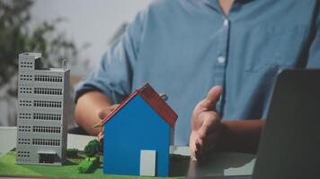 Man holding a model of a house and laptop in front of a building video