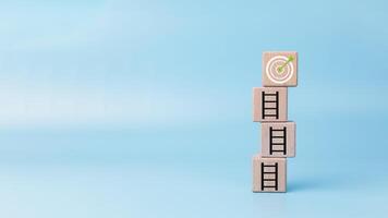 Target board on the top of ladder which print screen on wooden cube block, Setup achievement objective in business finance concept, White dartboard with arrow business objective and goal concept. photo