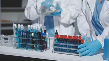 Two people in lab coats and gloves are working on a table video