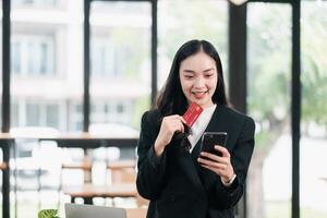 Smiling businesswoman using a smartphone and credit card for online shopping in a bright, modern office setting. photo