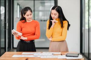 Two women in a modern office discuss a project, surrounded by documents and digital devices, showcasing teamwork and creativity. photo