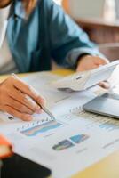 Close-up of a person using a calculator and reviewing financial charts and graphs on paper in an office environment. photo