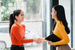 Two women in a modern office setting, shaking hands and smiling, symbolizing successful business collaboration. photo