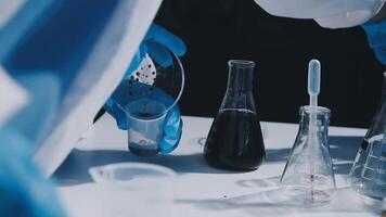 A person in a lab coat and gloves is pouring liquid into a beaker video