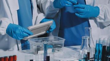Two people in lab coats and gloves are working on a device video