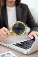 A business professional uses a magnifying glass to closely examine data on a laptop, symbolizing attention to detail and analysis. photo