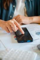 Hand interacting with smartphone on top of business papers featuring graphs and charts, highlighting technology in work. photo