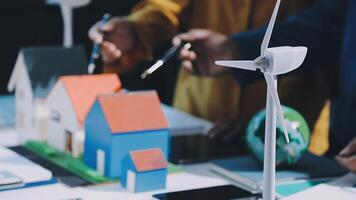 A group of people are working on a model of a house with wind turbines video