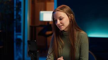 Happy girl arriving in studio, filming with smartphone on tripod, discussing topics of interest for gen Z fanbase. Jolly media star entering home studio, recording with mobile phone, camera A photo