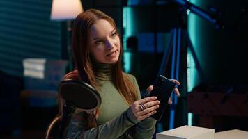 Gen Z content creator filming technology review of newly released smartphone, unpacking it and presenting specifications to audience. Internet star showing cellphone to fans from studio, camera A photo