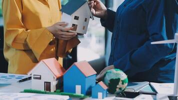 Two people holding a model house and a wind turbine video