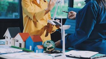 Two people standing around a table with a model house video