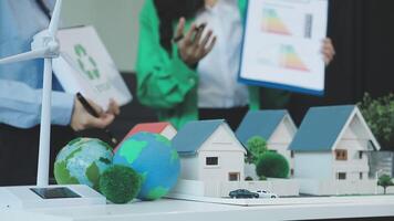 A woman is holding a paper with a model of a house and a wind turbine video