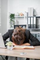 Tired businesswoman resting her head on a desk in an office setting, symbolizing stress and burnout. photo