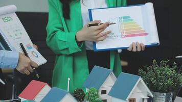 Two people are holding papers and a house model video