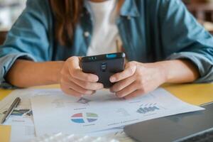 Close-up of hands using smartphone over financial documents with charts and graphs, showcasing business analysis and technology. photo