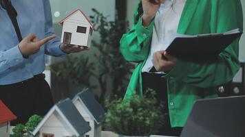 Two people holding a house model and a laptop video